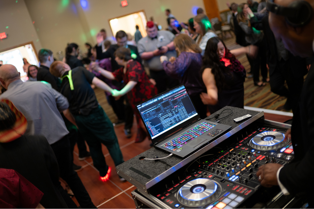 DJ equipment at prom with students on the dance floor in the background.