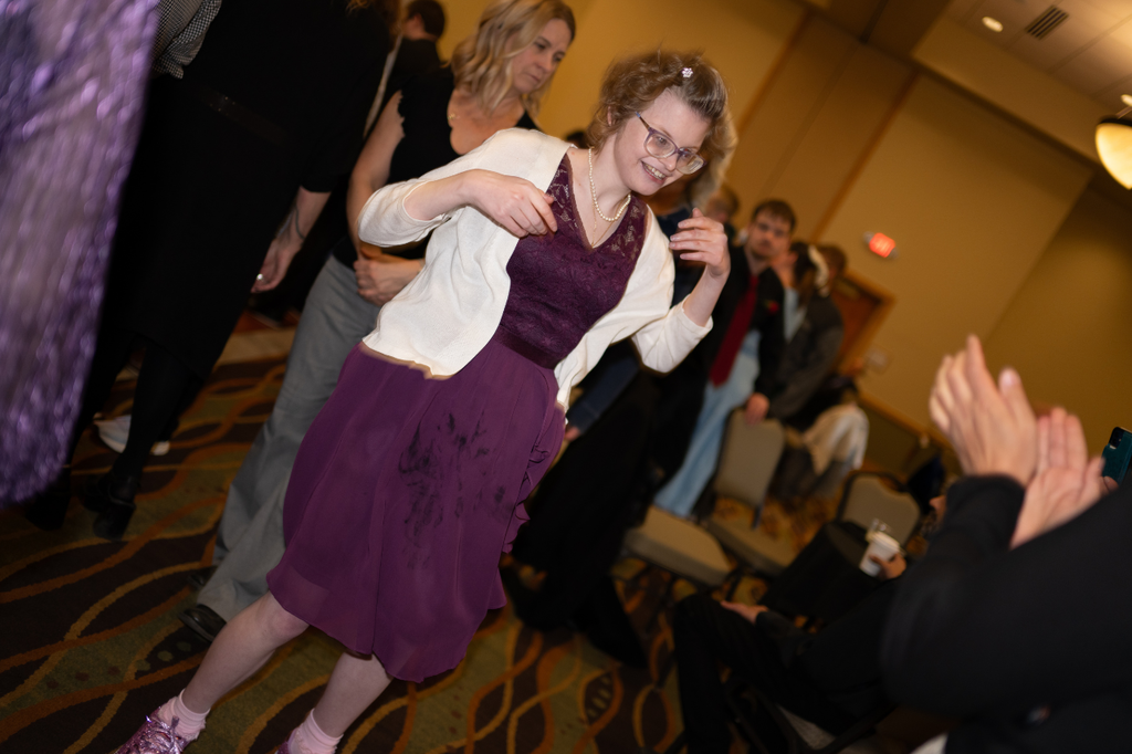 Transition Campus student wearing a purple dress and white cardigan smiling and dancing on the prom dance floor.