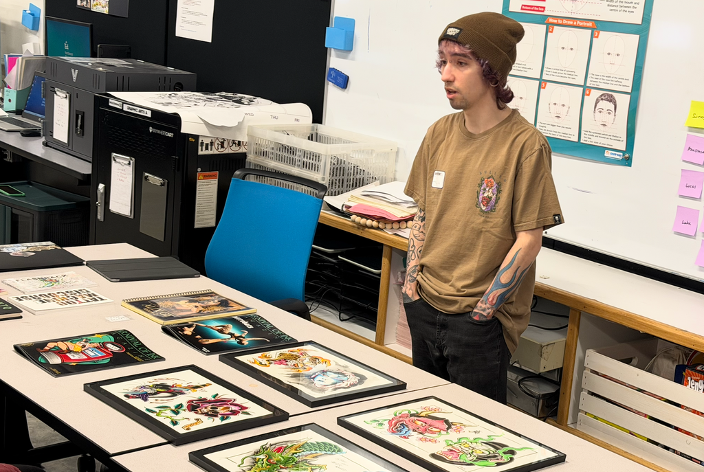 Tony Diaz standing by a table where portfolio art is displayed.