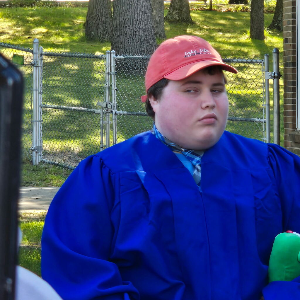 2026 Bridgeway Program graduate wearing an orange baseball cap and blue gown for the ceremony. 