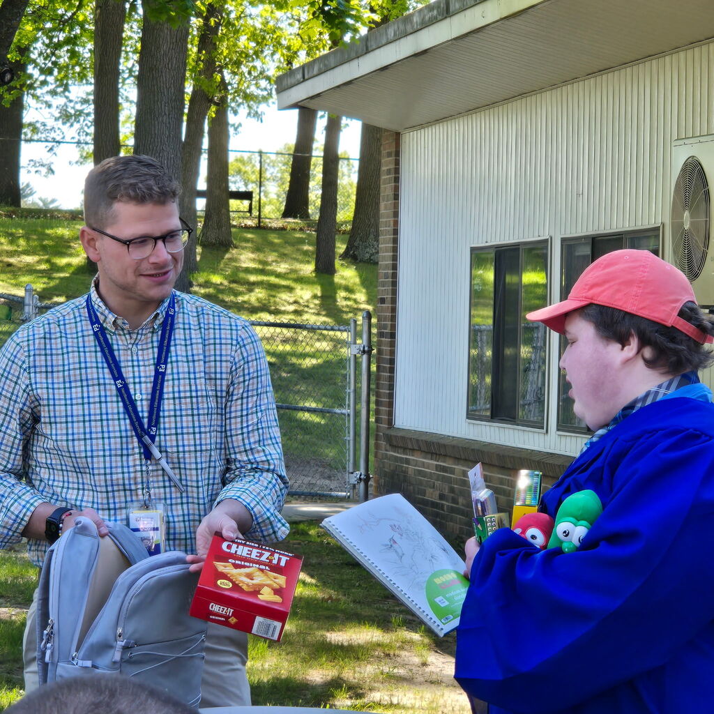 2026 Bridgeway Program graduate holding multiple gifts as a staff member hands them a Cheez-It box. 