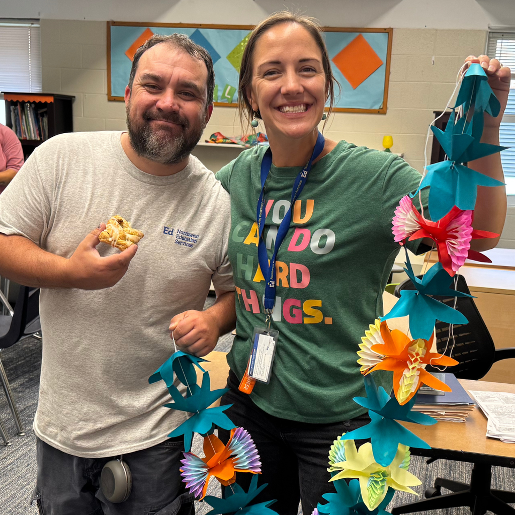 North Ed staff members holding a breakfast pastry and colorful paper garland pose together for a photo inside of a classroom.