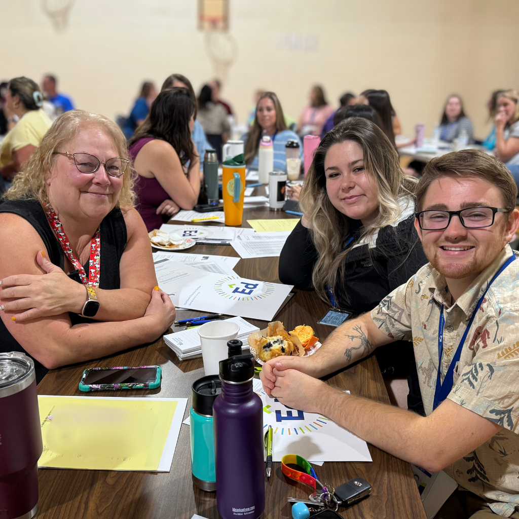 Three North Ed Bridgeway staff members sitting on lunch tables in a crowded gymnasium on Opening Day.