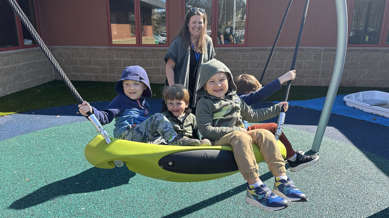 A woman pushes children on a group swing on the playground at the Joseph C. Fisher Early Childhood & Family Center at Northwest Education Services.