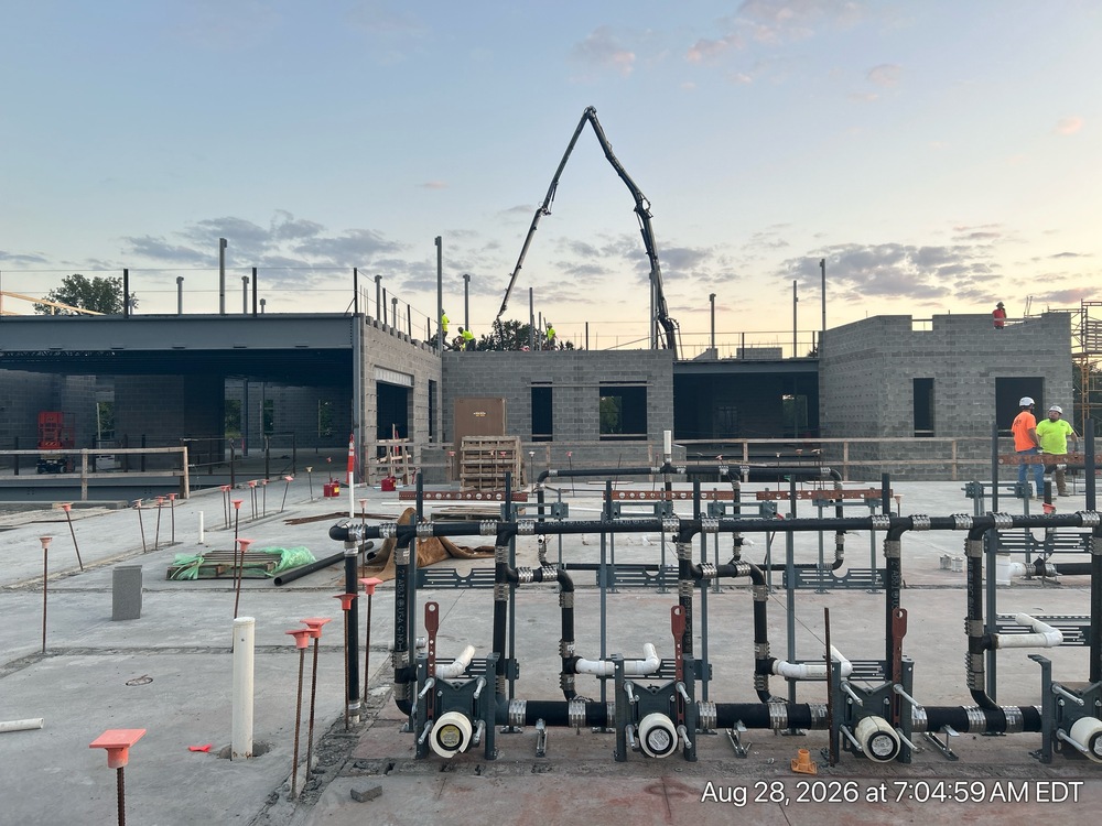 This month brings exciting progress! Crews are pouring the concrete floor for the top-floor classroom wing, and the walls for the lower level are starting to go up. Behind the scenes, the building's "nervous system" — its electrical wiring, plumbing, and heating/cooling systems — is being installed throughout the ceilings and walls. Meanwhile, block walls are being built in what will be the Kitchen and Special Education areas. Outside, things are taking shape too: new sidewalks are being poured, and light poles are going up around the future parking lots to help light the way.