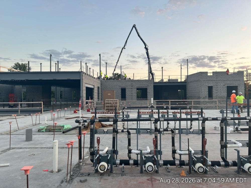 This month brings exciting progress! Crews are pouring the concrete floor for the top-floor classroom wing, and the walls for the lower level are starting to go up. Behind the scenes, the building's "nervous system" — its electrical wiring, plumbing, and heating/cooling systems — is being installed throughout the ceilings and walls. Meanwhile, block walls are being built in what will be the Kitchen and Special Education areas. Outside, things are taking shape too: new sidewalks are being poured, and light poles are going up around the future parking lots to help light the way.