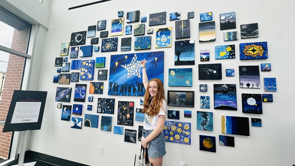 Photo of a student standing in front of the artwall, being interviewed by the news.