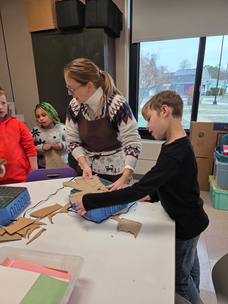student cutting his design with teacher guiding