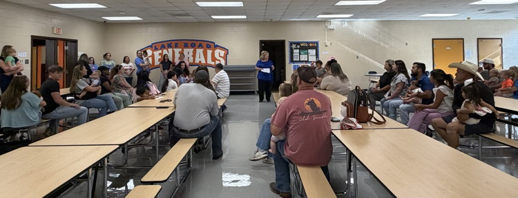 A group of parents and their children in the LRS cafeteria listening to Academy details from staff.