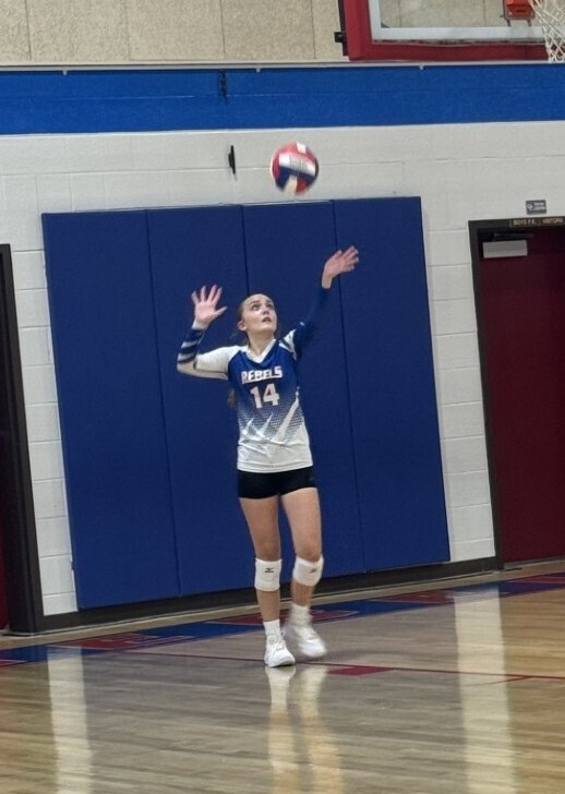 A volleyball player in uniform jumps to serve a volleyball in a gym.