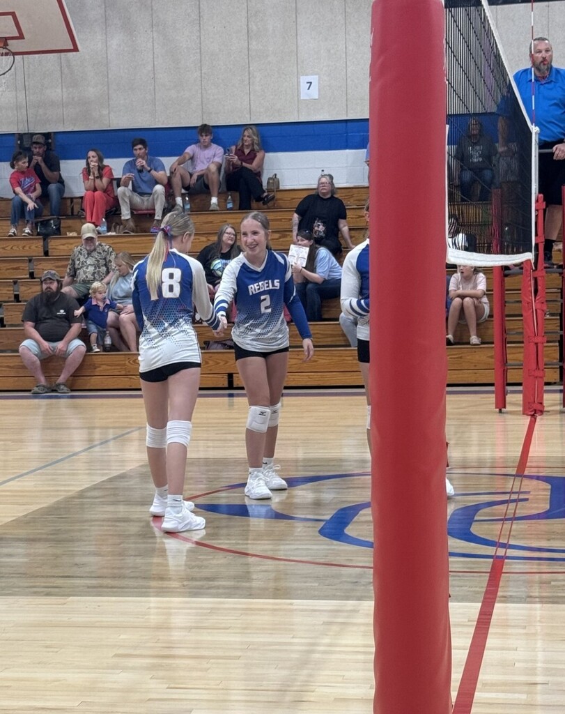 Two volleyball players in uniform standing on an indoor court during a game.