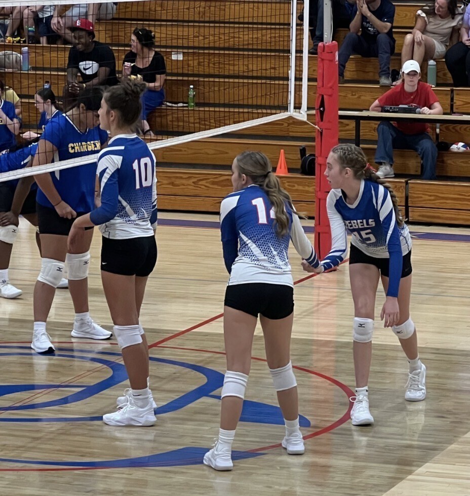 Girls in blue-and-white volleyball uniforms stand on the court during a game.