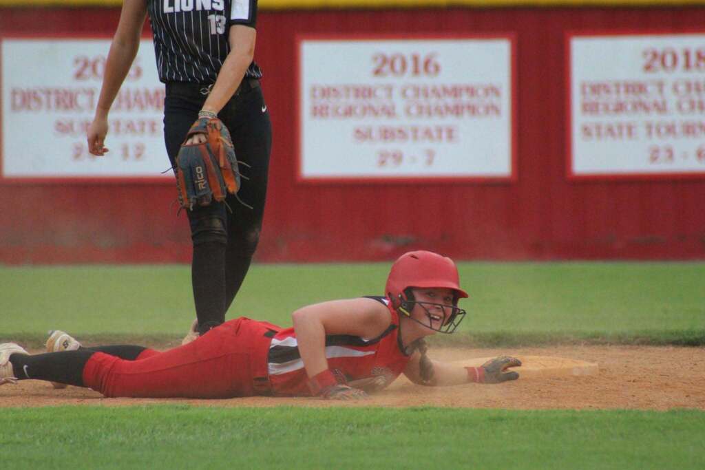 A softball player in a red uniform slides into home plate during a game.