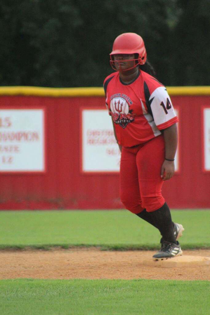 A softball player in a red uniform and helmet standing on the field.