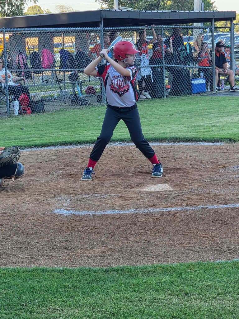 A young softball player at bat, holding a bat over their shoulder on a softball field.