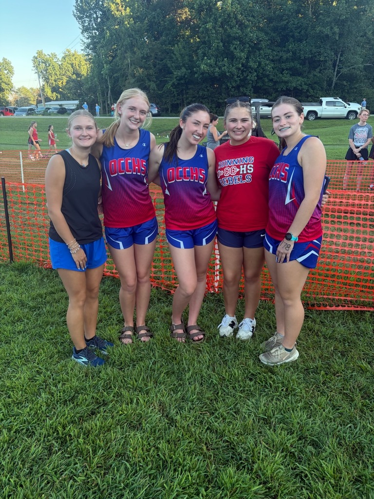 OCCHS girls cross country runners pose together after the Dresden Invitational, standing near the course finish area in their team uniforms and a “Running OCCHS Rebels” shirt.