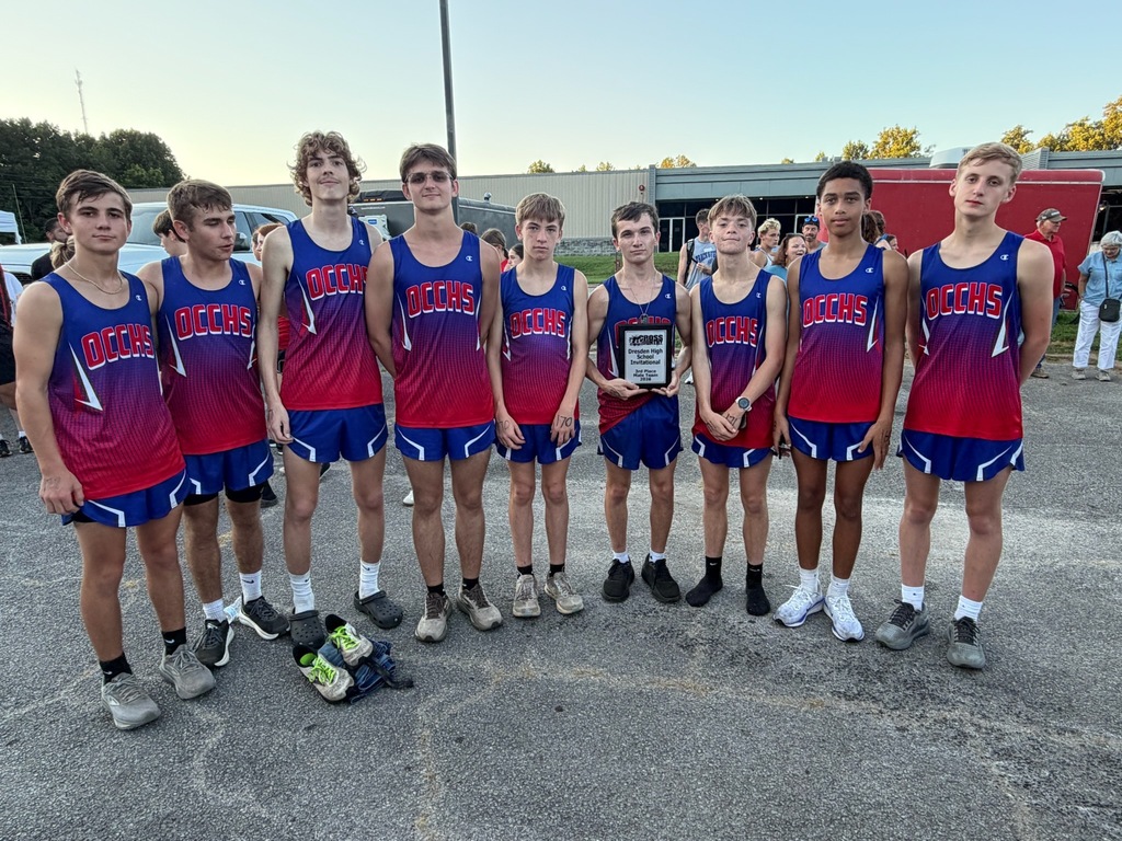 OCCHS boys cross country team poses with their third-place team plaque following the Dresden Invitational. Eight runners stand together in their blue and red uniforms, with one team member holding the award.