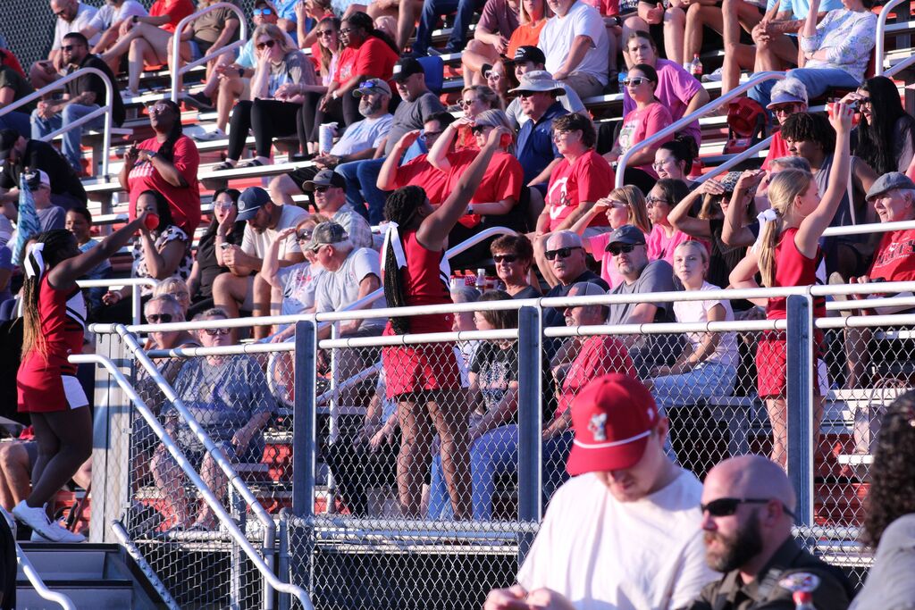 Cheerleaders in red uniforms lead a cheer in the bleachers during football game.