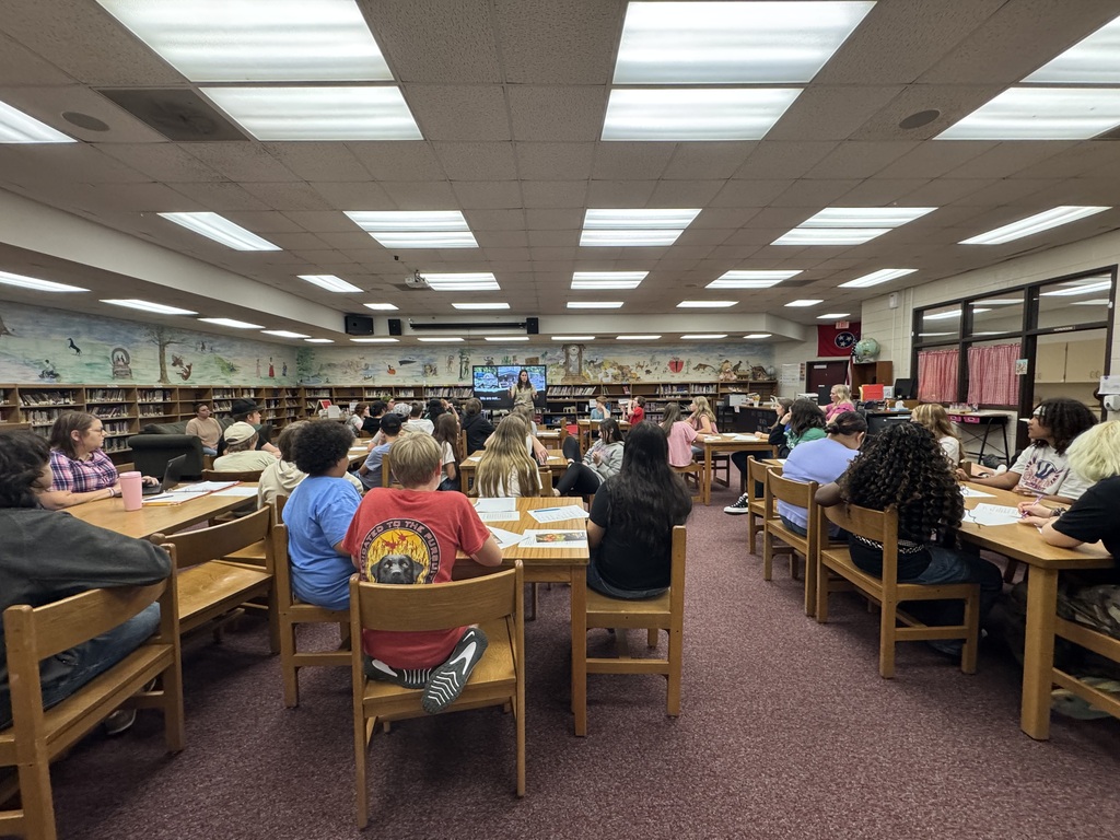 Image of various students sitting at tables listening to a speaker.