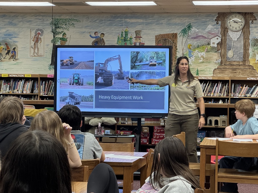 Image of a woman, Tara Dowdy, showing a picture of heavy equipment to a group of students.