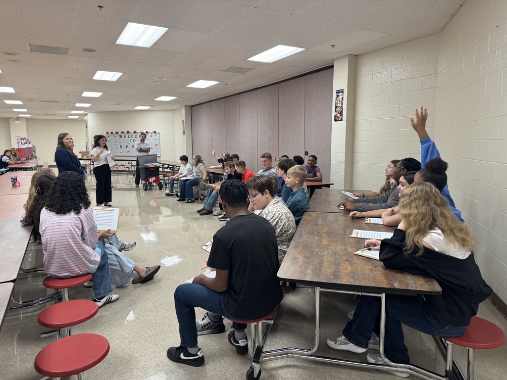 Students participate in South Fulton Middle School’s Financial Fair as they listen to instructions and prepare to complete budgeting activities. One student raises a hand while others review their worksheets during the hands-on financial literacy experience.