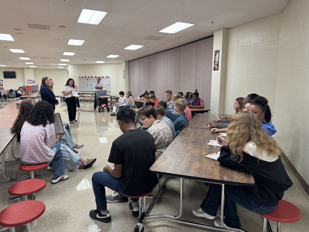 Students listen as a facilitator gives instructions during South Fulton Middle School’s Financial Fair. Students sit at cafeteria tables with budgeting worksheets and prepare to complete hands-on activities focused on financial decision-making and budgeting.