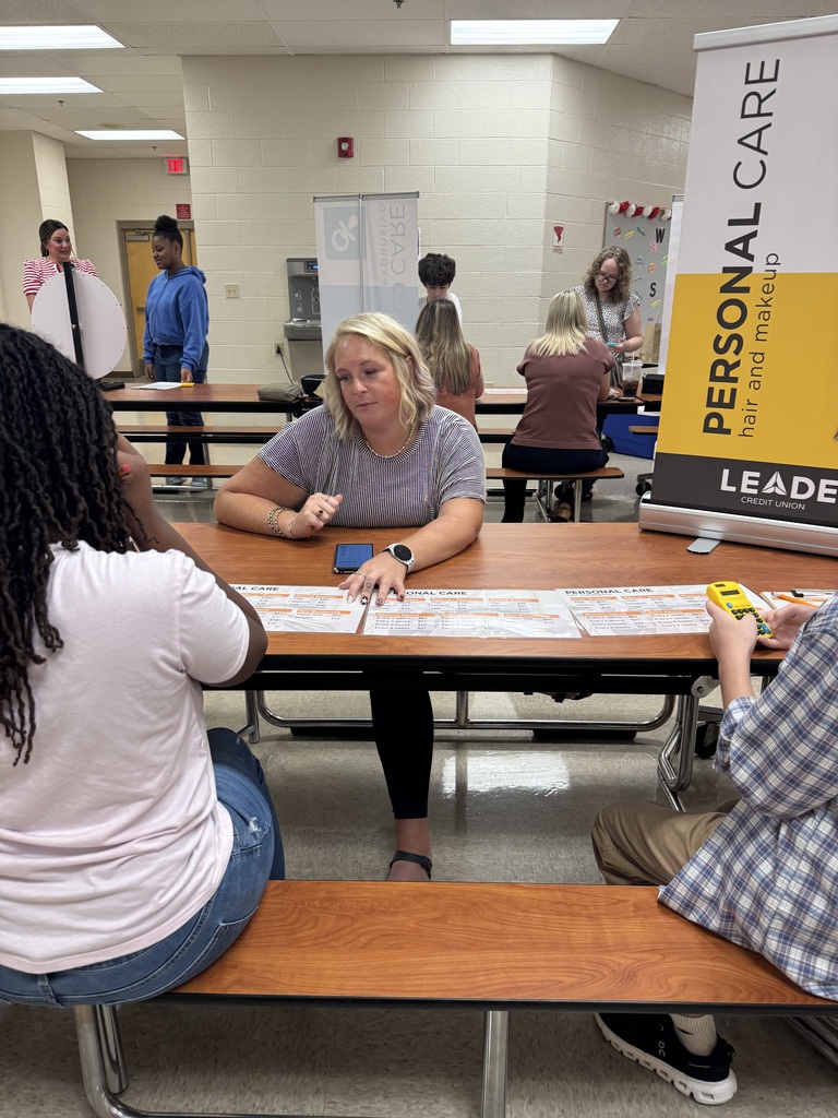 A South Fulton Middle School student participates in the Financial Fair by discussing financial decisions with a facilitator at a personal-care budgeting station. Other students work at nearby stations as they complete the hands-on financial literacy activity.