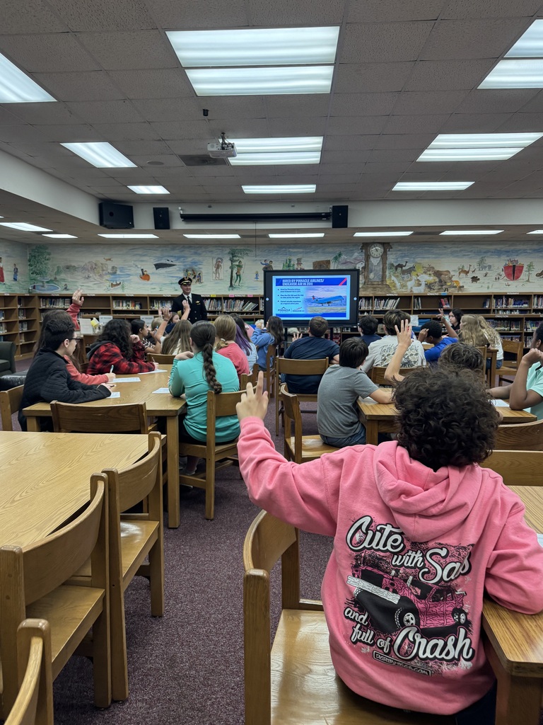 7th grade students sitting with hands raised to answer questions.