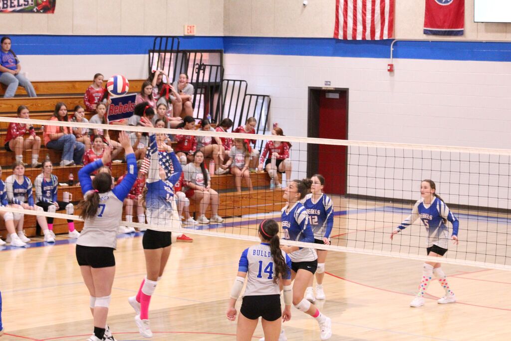 OCMS Volleyball player taps the ball over the net during a volleyball game while other players watch.