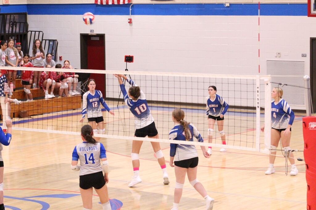 OCMS Volleyball player hits the ball over the net while other players look on.