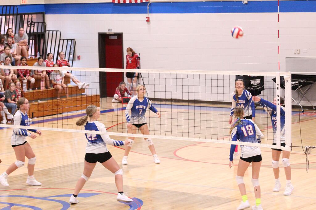 OCMS Volleyball player hits the ball over the net while other players watch.