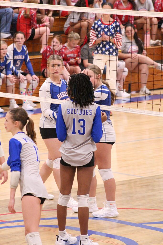 OCMS players and opponents stand at the net, awaiting a serve, during a volleyball game.