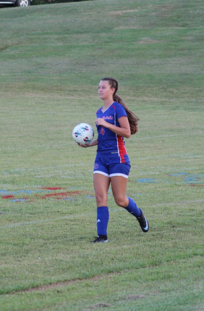 A girls soccer player in a blue uniform carries the ball across the field during a game.