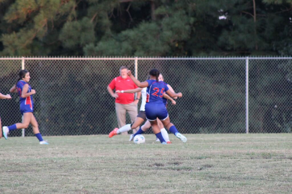 Girls soccer players in blue and white uniforms compete for possession of the ball during a game on a grassy field.