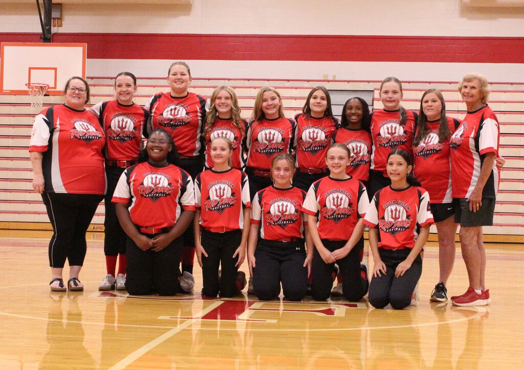 South Fulton Red Devils softball players and coaches pose for a team photo in a school gym. The group wears matching red-and-black uniforms and stands in two rows on the basketball court.