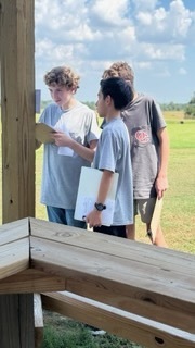 Three OCMS students stand outside working together and reviewing their papers.