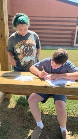 Two OCMS students work together on a written class activity outside.