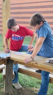 Two OCMS students work together on an outdoor class activity at a wooden table.