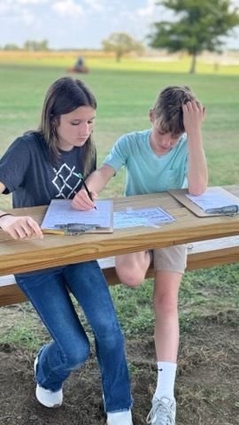 Two OCMS students sit at an outdoor table and work together on a class assignment.