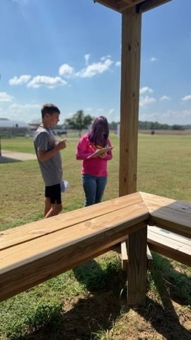 Two OCMS students stand outside completing an activity using clipboards.