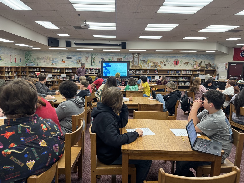 A wide view of OCMS students gathered in the library for a career presentation about physical therapy. Students listen as the guest speaker presents information on the screen.