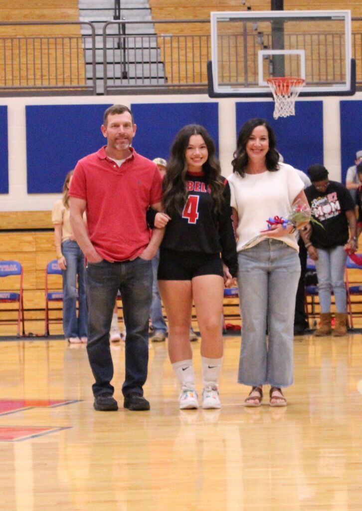 Volleyball player in Rebels jersey #4 stands with two family members on a gym court during senior night recognition.