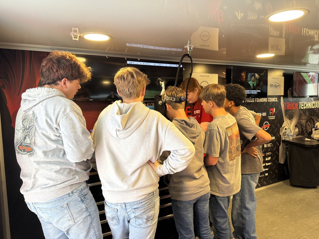 Students gather around a hands-on workstation inside the Be Pro Be Proud mobile workshop, watching a demonstration with a student ambassador.