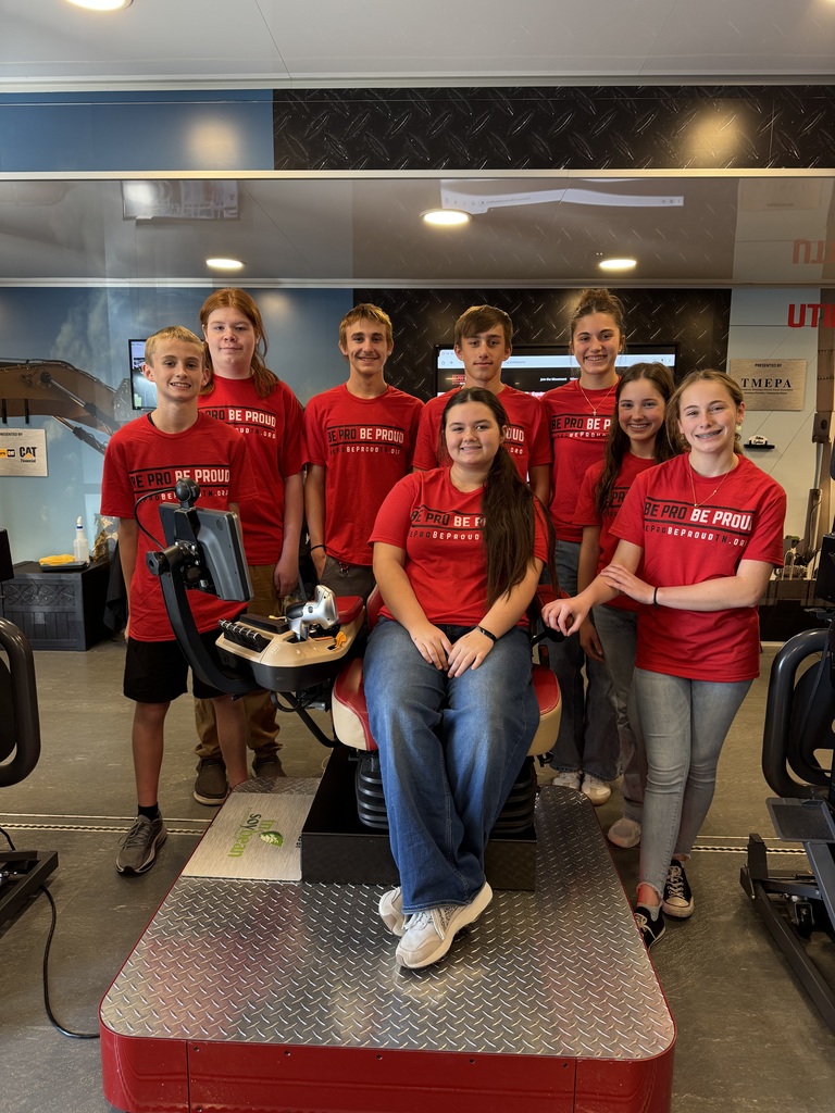 Student ambassadors wearing red Be Pro Be Proud shirts pose together around a simulator chair inside the mobile workshop.