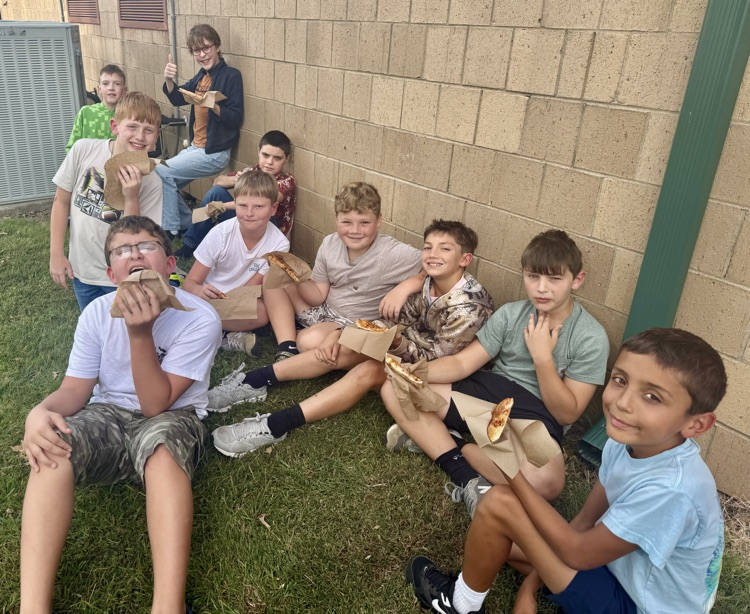 group of students sitting in grass eating pizza 