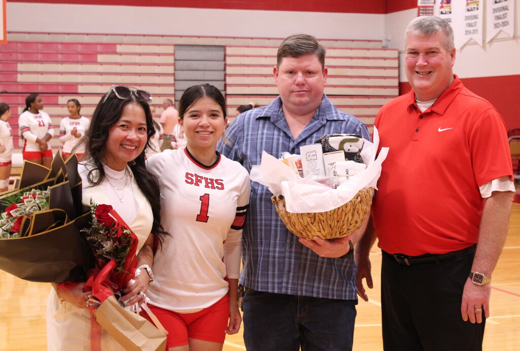A South Fulton Volleyball player smiles with her parents and coach while holding flowers and gifts from her team.