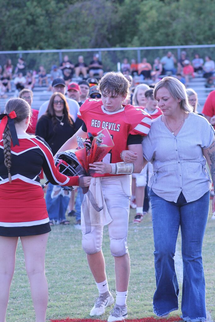 A SFMS football player accepts flowers from a cheerleader while being escorted by his Mom.