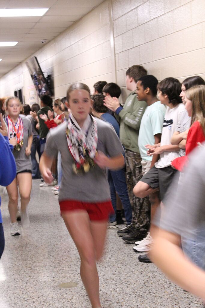 An OCMS Cross Country runner runs the hallway that is lined by students cheering.