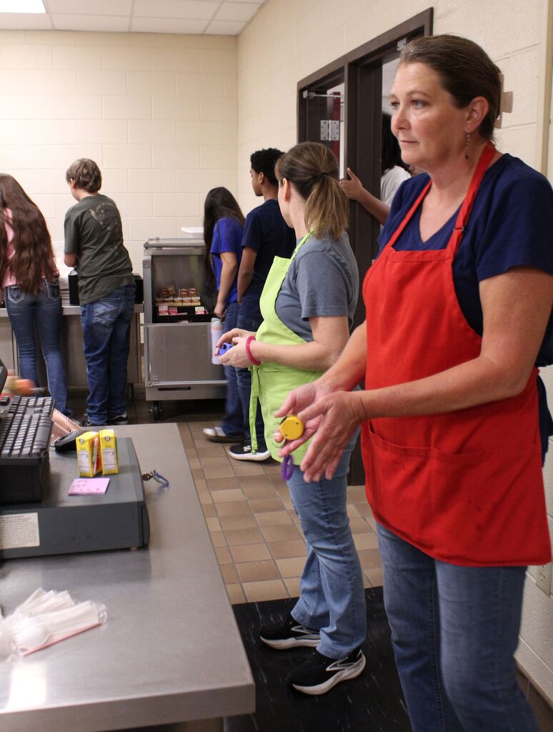 Two cafeteria students oversee and assist students in preparing their lunch trays.