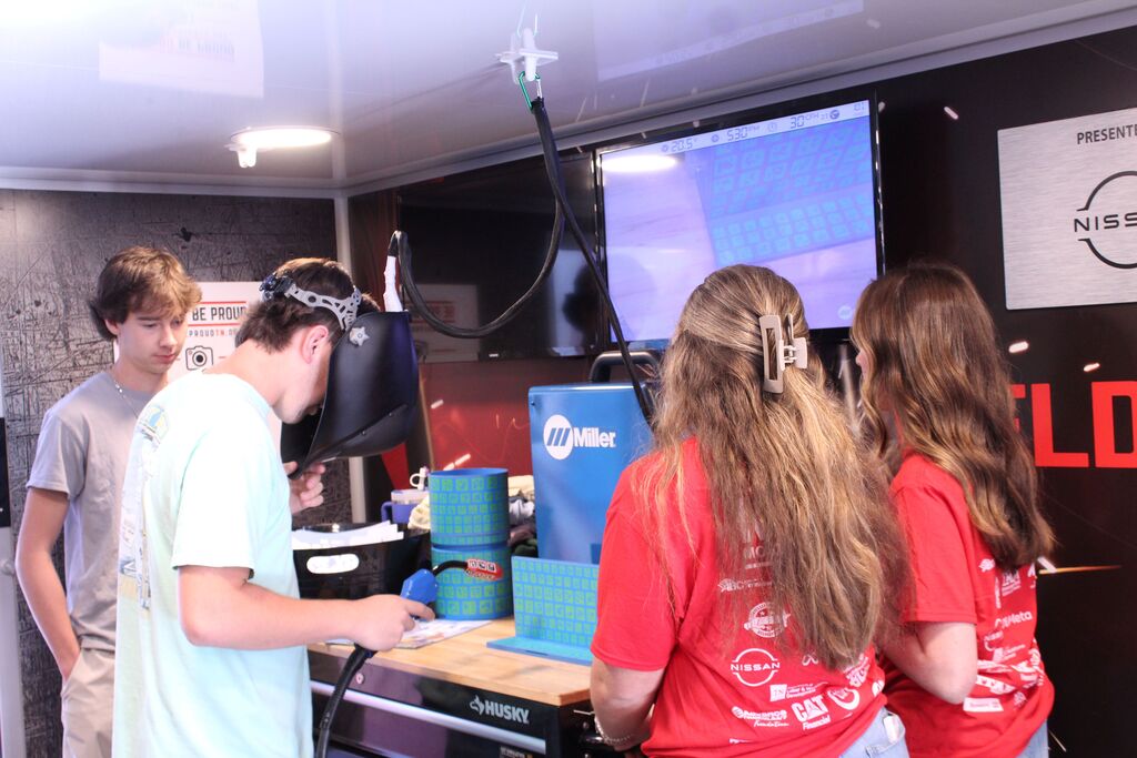 A group of students look on as another student tries the welding simulator or the Be Pro, Be Proud truck.